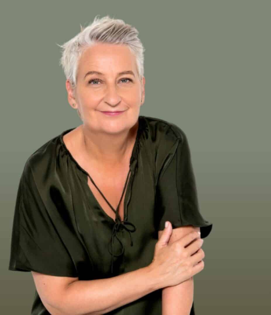 Rikke winckler from forældesparring. Dk with short gray hair and a green blouse smiles against a plain background, embracing the excitement of 2024 like they're ready for a sparring session in life's ring.