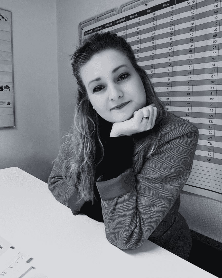Gyde Balzer Carstensen in a blazer sits at her desk, resting her chin on her hand, with a calendar marking key dates for IP strategy in the background. Her gaze meets the camera in this captivating black and white image.